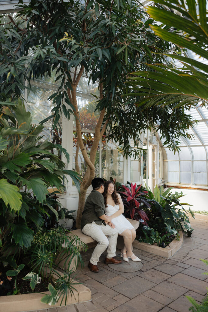 True to life engagement photo of a couple at Buffalo botanical gardens with soft natural light and florals